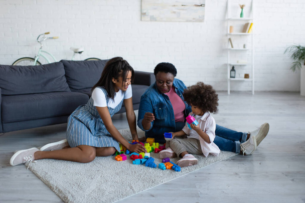 african american women playing building blocks game with toddler girl on floor at home - Fotoğraf, Görsel