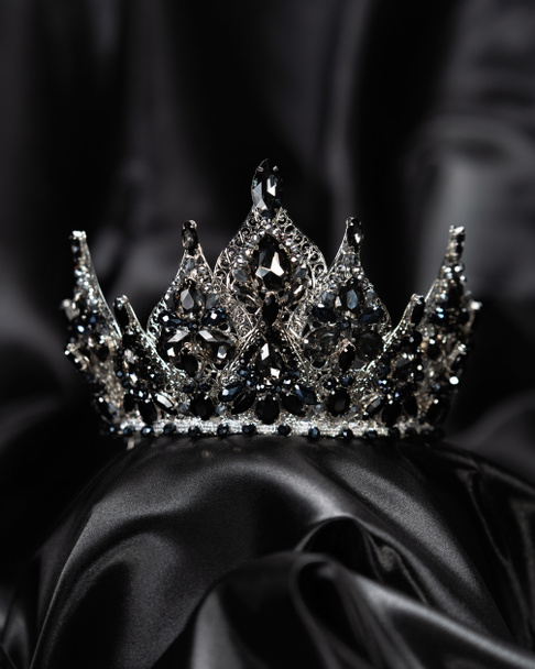 Corona para la señorita belleza, un símbolo de poder y elegancia, competencia, espectáculo. Tiara en metal blanco y piedras negras sobre fondo satinado negro - Foto, Imagen