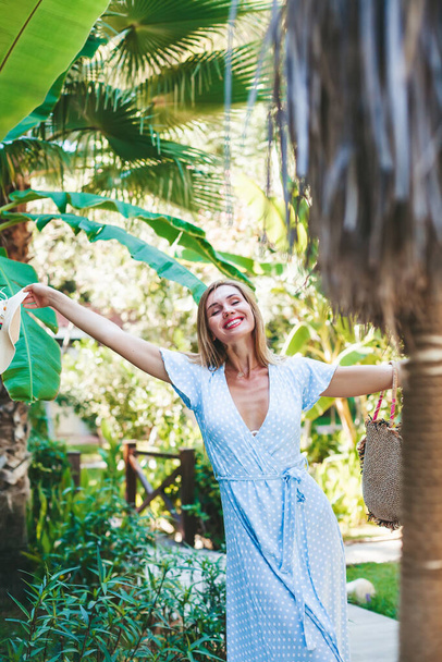 Beautiful young woman in a blue long dress feeling happy and free in a green tropical garden - Foto, imagen
