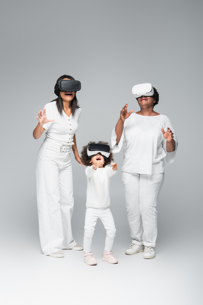 middelbare leeftijd Afrikaanse Amerikaanse vrouw met dochter en kind gaming in vr headsets op grijs - Foto, afbeelding