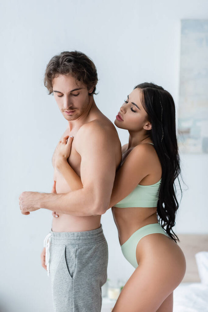 Seductive woman in underwear embracing shirtless boyfriend at home  - Photo, image