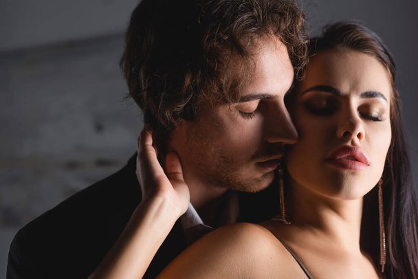 Man in formal wear kissing seductive girlfriend at home at night  - Foto, Imagen