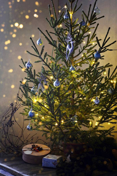 Albero di Natale decorato con luci e giocattoli di vetro nella stanza (stanza) con regali. Sfondo scuro con luci, umore festivo. - Foto, immagini