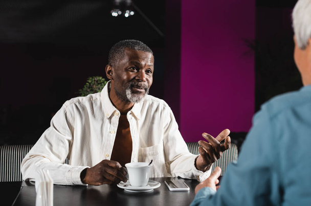 senior african american man gesturing during conversation with blurred friend in pub - 写真・画像
