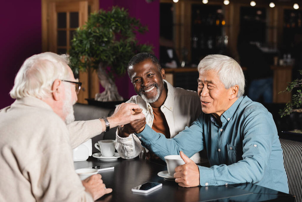 щасливі старші багатоетнічні друзі, що приєднуються до рук, сидячи в кафе
 - Фото, зображення
