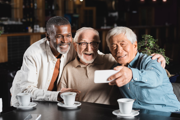 senior aziatische man het nemen van selfie met gelukkig multi-etnische vrienden in restaurant - Foto, afbeelding