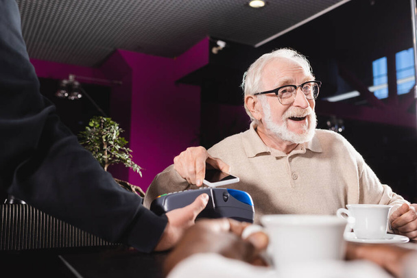 senior en lunettes payer avec smartphone via terminal de paiement dans pub - Photo, image