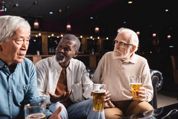 афроамериканський чоловік жестикулює під час розмови з старшими міжрасовими друзями в пабі
 - Фото, зображення