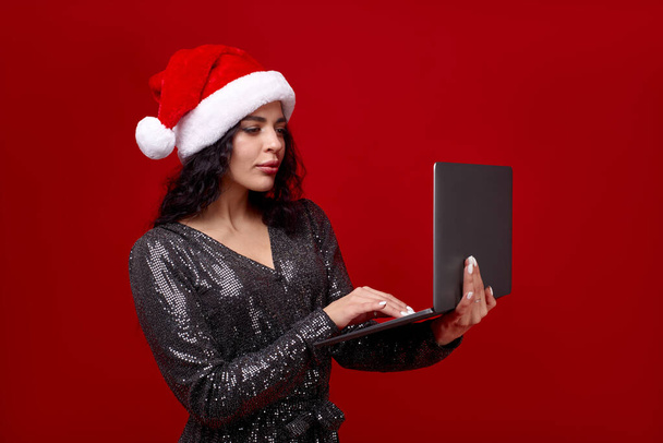 Una mujer con gorra navideña sostiene un portátil - Foto, Imagen