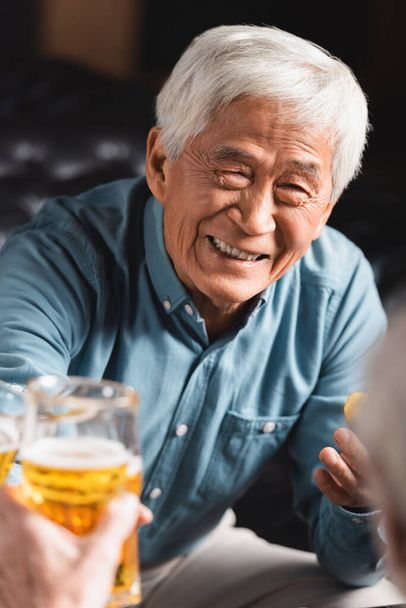 allegro anziano asiatico uomo clinking occhiali di birra con offuscata amico in pub - Foto, immagini