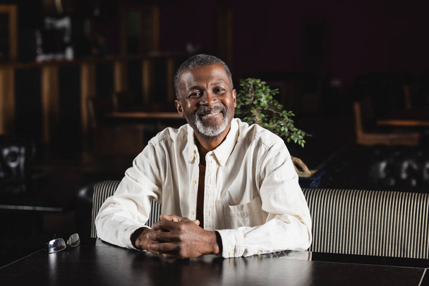 cheerful senior african american man sitting in pub and looking at camera - Photo, Image