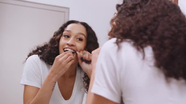 Zdravé multikulturní mladá dospělá žena zubní nit v moderním koupelnovém zrcadle - Záběry, video