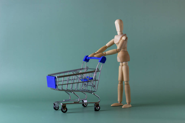 Speelgoedmodel van een houten man met een trolley. Ga winkelen concept. Mockup voor reclame van geschenken, kleding, winkelen. - Foto, afbeelding
