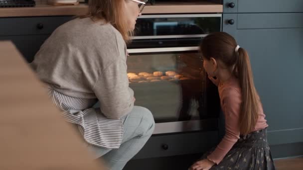 Großmutter und Enkelin warten neben dem Ofen auf selbstgebackene Plätzchen. Aufnahme mit roter Heliumkamera in 8K    - Filmmaterial, Video