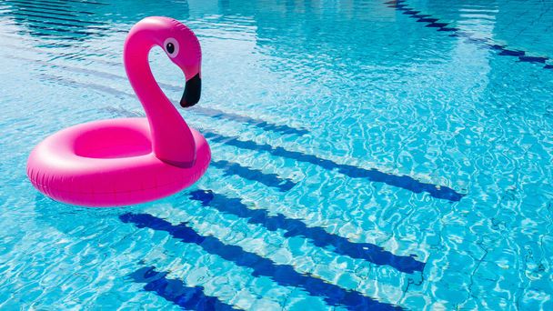 フラミンゴのプラスチック。ビーチの背景のためのプール水にピンクのインフレータブルフラミンゴ。流行の夏のコンセプト - 写真・画像
