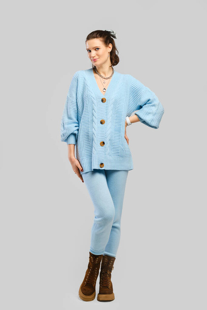 Full length portrait of beautiful woman in light blue warm knitted tracksuit over grey background - Foto, afbeelding