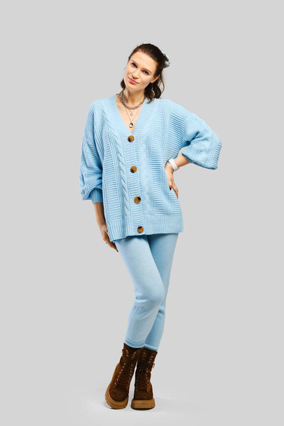 Full length portrait of beautiful woman in light blue warm knitted tracksuit over grey background - Photo, image