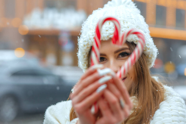 Hermosa mujer joven sosteniendo caramelos de Navidad en la ciudad en forma de corazón. Espacio para texto - Foto, imagen