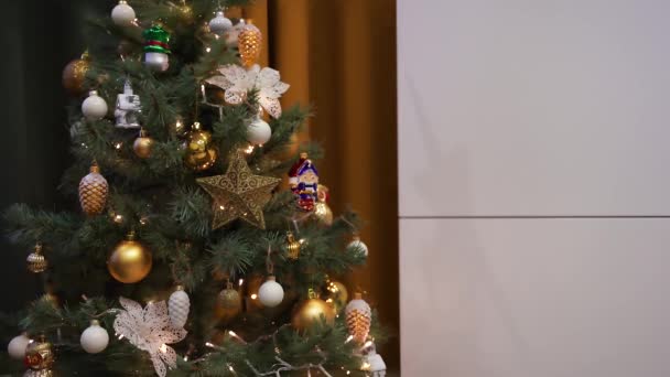 Prachtige versierde kerstboom met bloemenslinger in de woonkamer. Gezellige winteravond. 4k video. - Video
