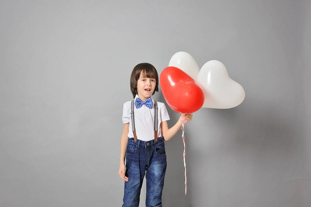 adorable niño caucásico sonriendo, sosteniendo globos en forma de corazón y mirándolos. El concepto de infancia y felicidad. - Foto, imagen