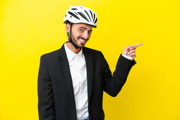 Ділова біла людина з велосипедним шоломом ізольовано на жовтому тлі вказуючи пальцем на бік
 - Фото, зображення