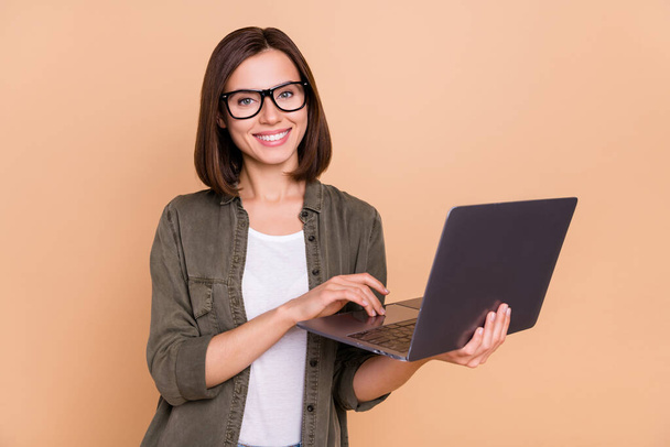 Photo of cheerful glad lady hold laptop prepare project wear eyewear khaki shirt isolated beige color background - Photo, image