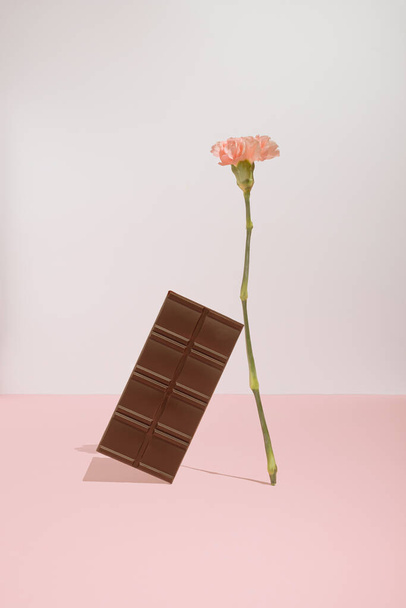Trendikäs Ystävänpäivä konsepti suklaapatukka ja vaaleanpunainen kukka pastelli taustalla. Moderni esteettinen. - Valokuva, kuva