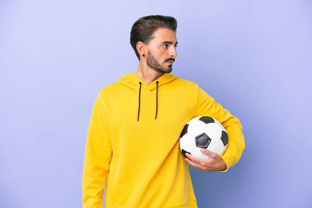 Giovane uomo caucasico isolato su sfondo viola con pallone da calcio - Foto, immagini