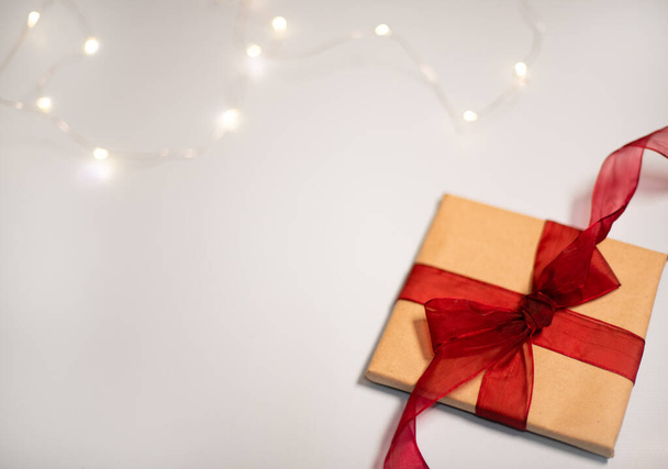 Подарок на белом. Подарок упакован в ремесленную бумагу с украшением рождественских огней - Фото, изображение
