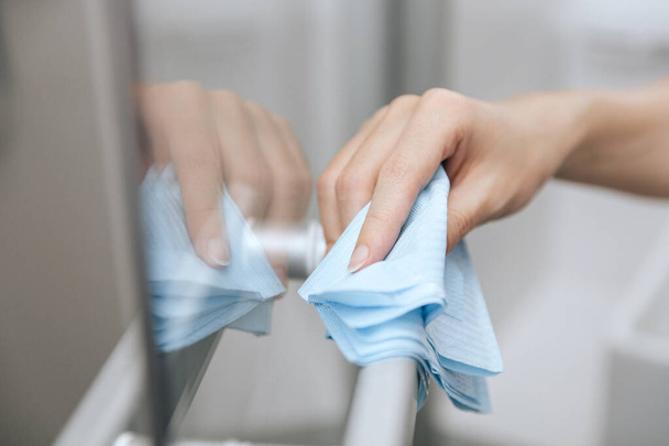 Cleaning glass door handles with an antiseptic wet wipe. Sanitize surfaces prevention in hospital and public spaces against corona virus. Woman hand using towel for cleaning home room door link - Photo, Image