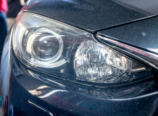 Close-up front headlight with xenon light of black modern car on grey background  - Фото, зображення