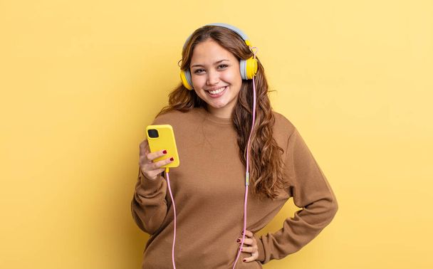 hispanic pretty woman smiling happily with a hand on hip and confident. headphones and smartphone concept - Foto, imagen