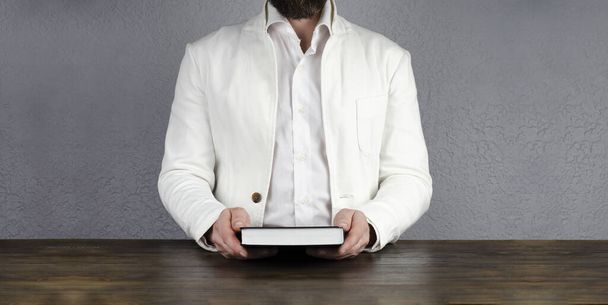 Ένας άντρας με σακάκι κρατάει ένα φάκελο βιβλίου ένα τάμπλετ. Νέος επιχειρηματίας. - Φωτογραφία, εικόνα