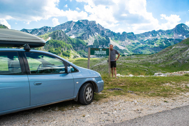 Turista cerca de firmar con la inscripción Durmitor y coche en bachround de hermosos picos de montaña. Parque Nacional Durmitor. Paso de carretera más alto de Montenegro, situado en el norte de Montenegro. - Foto, Imagen