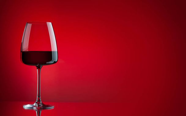 Rood wijnglas over rode achtergrond met kopieerruimte - Foto, afbeelding