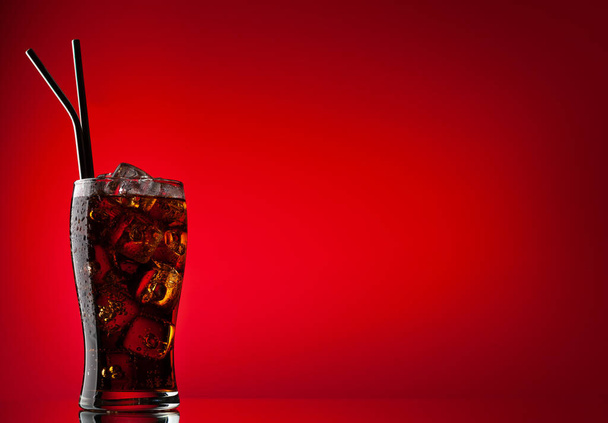 Cola con hielo. Bebida dulce fría fresca con cubitos de hielo. Sobre fondo rojo con espacio de copia - Foto, Imagen