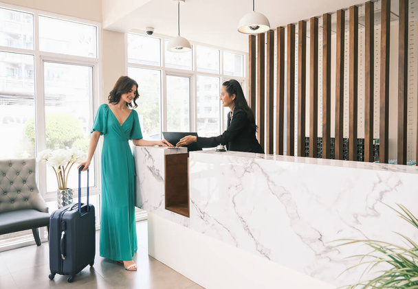 Ázsiai lány recepciós és kaukázusi nő utazó ellenőrzés vagy pénztár a szállodában - Fotó, kép