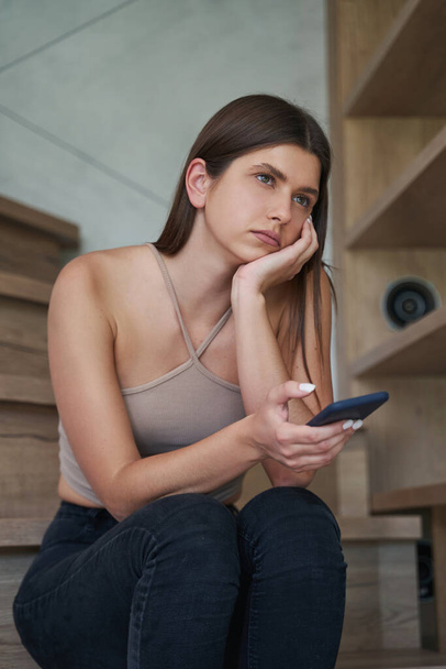 Dejected woman with smartphone sitting on stairs - Foto, imagen