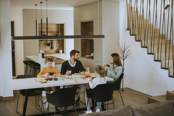 Familie benutzt Mobiltelefone beim Frühstück am Esstisch in der Wohnung - Foto, Bild
