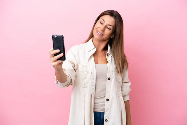 Middelbare leeftijd blanke vrouw geïsoleerd op roze achtergrond het maken van een selfie - Foto, afbeelding