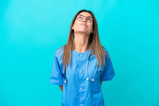 Middle age surgeon woman isolated on blue background and looking up - Fotografie, Obrázek