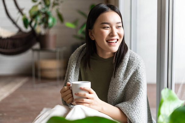 Felice donna asiatica ridere e sorridere, seduto sul pavimento a casa vicino alla finestra e godersi il fine settimana, giornata di relax - Foto, immagini