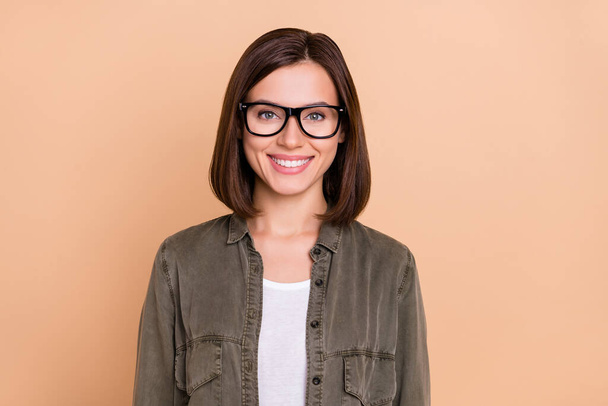 Φωτογραφία από θετική γοητευτική κυρία λαμπερό χαμόγελο toothy φορούν γυαλιά χακί πουκάμισο απομονωμένο μπεζ χρώμα φόντο - Φωτογραφία, εικόνα
