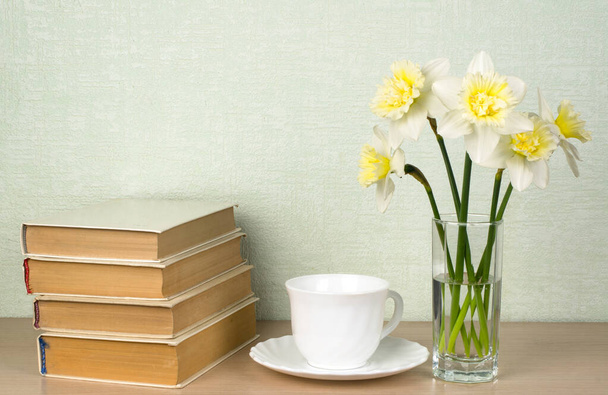 Daffodils, um copo branco e um pires, livros. Leitura de conceitos, literatura clássica. Lugar para texto, espaço de cópia - Foto, Imagem