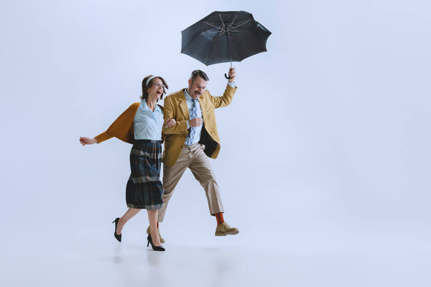 Young happy family couple, man and woman in retro style clothes, fashion of 70s, 60s years walking with umbrella isolated on white studio background - Fotografie, Obrázek