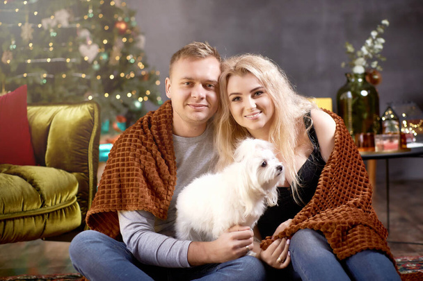 Szép romantikus pár ünnepi esztétikai hangulatos belső tér kutyájukkal közel karácsonyfa. Őszinte, igazi pillanat. Jó hangulat és szórakozás együtt. Karácsonyi szerelem. - Fotó, kép