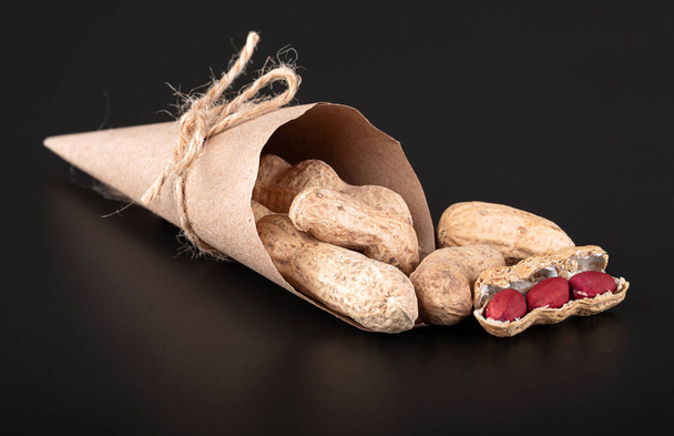 Peanuts in a craft bag on a black background with reflection - Photo, Image