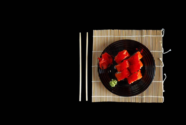 suosittua ruokaa. sushia, inkivääriä mustalla lautasella. Tarjoillaan lautasen japanilainen tyyli. Sushi syömäpuikot levy rullina ja bambu matto eristetty mustalla pohjalla. - Valokuva, kuva