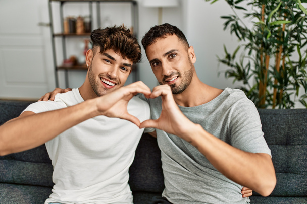 Two hispanic men couple smiling confident doing heart shape with hands at home - Photo, image