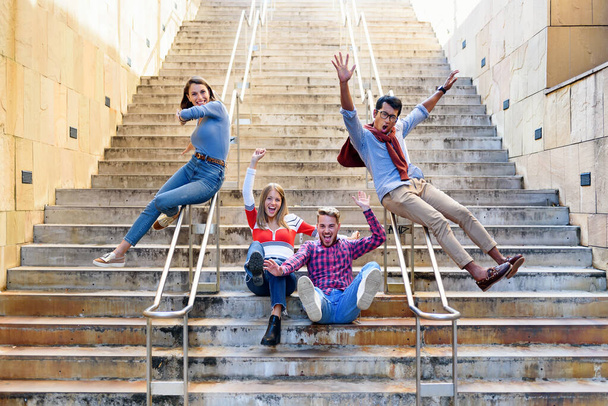 Grupo multicultural de amigos felizes animados aplaudindo e rindo enquanto deslizam pelos trilhos de um lance de escadas externas em uma cidade em um conceito de liberdade e estilo de vida ativo - Foto, Imagem